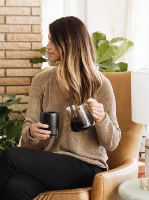Nő bézs pulóverben, kezében barista eszpresszó kiöntő üvegből, modern dizájn, Legfrissebb hírek, minden a kávéról.